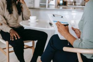 Two people sitting at a table reviewing performance on a clipboard over coffee.