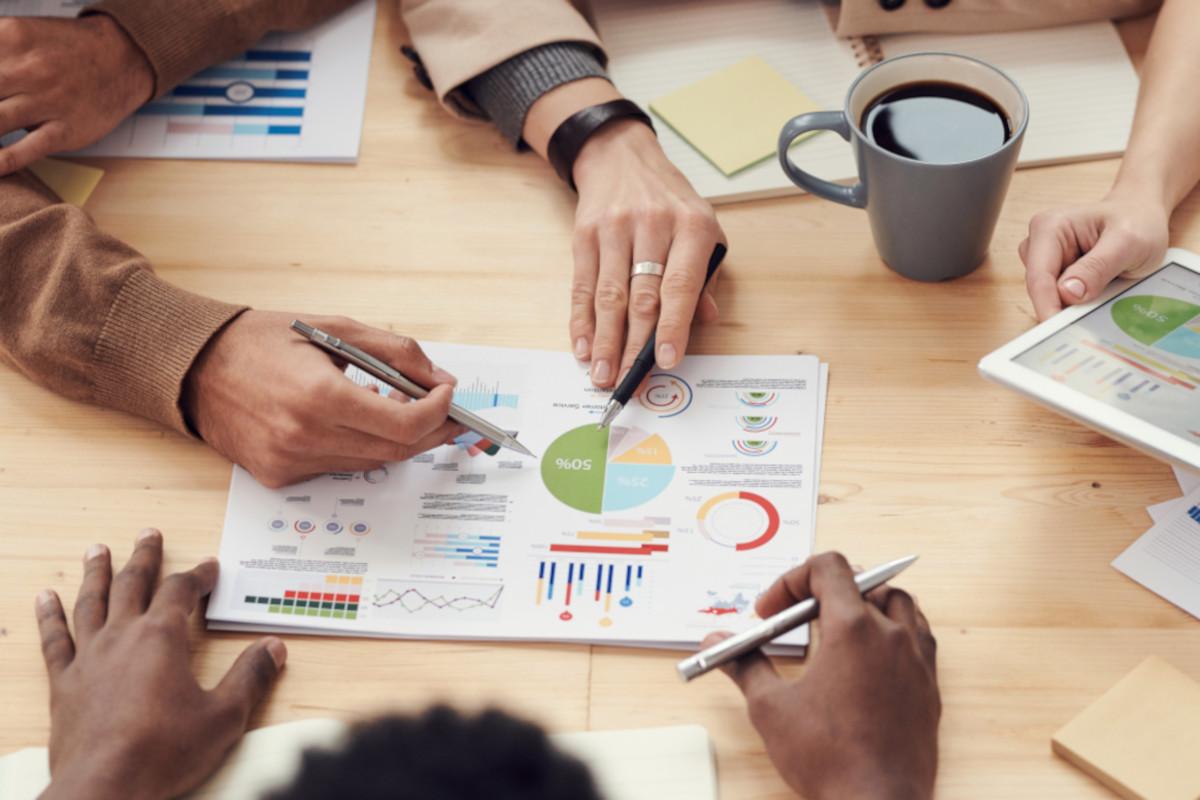 Close up of people's hands reviewing a document containing various charts and graphs on a boardroom table