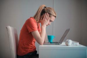 A woman hunched over a laptop looking defeated.