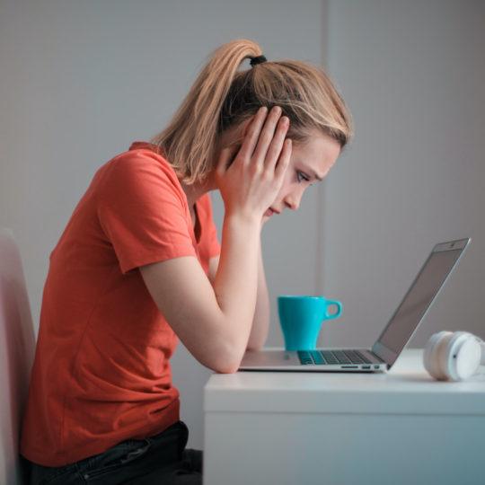 A woman hunched over a laptop looking defeated.